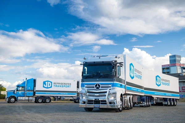Two JD prime movers with refrigerated trailers parked in the yard