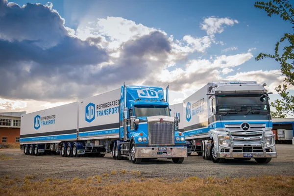 A JD Kenworth B-double and a Mercedes-Benz prime mover side by side under a big sky